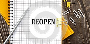 REOPEN text on a sticker on the notebook, wooden background