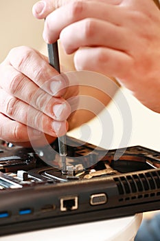 Repaiman with screwdriver fixing disassembled laptop parts. Technical support and fixing gadgets problems. Servicing
