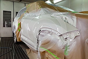 Repainting the damaged front part of an expensive SUV vehicle in white in a professional auto repair shop using paintwork