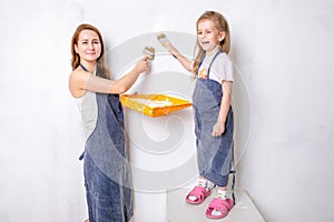 Repair in the apartment. Happy family mother and little daughter in blue aprons paints the wall with white paint