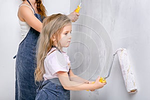 Repair in the apartment. Happy family mother and little daughter in blue aprons paints the wall with white paint. Daughter paints