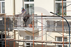Repair of the balcony and facade of the building. The builder stands on the balcony and holds a sheet of glass and tools in his