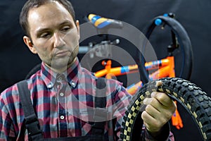 Repair of a children's bicycle in the workshop. The mechanic holds an old punctured tire with a hole in his hand.