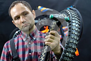 Repair of a children's bicycle in the workshop. The mechanic holds an old punctured tire with a hole in his hand.