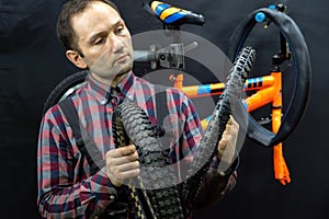 Repair of a children's bicycle in the workshop. The mechanic holds an old punctured tire with a hole in his hand.