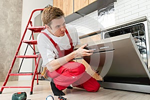 Repair of dishwashers. Repairman repairing dishwasher in kitchen