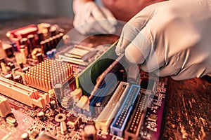 A repair engineer holds a RAM chip with his hands, inserts the RAM into the socket of the computer`s motherboard