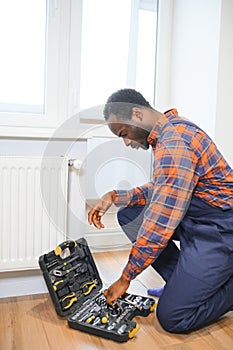 Repair heating radiator close-up. African man repairing radiator with wrench. Removing air from the radiator