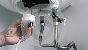 Repair and maintenance of boilers. The hand of a plumber installs a thermostat in a boiler after repair. Water heater repair