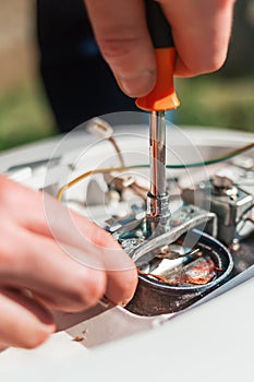 Repair and maintenance of the water heater. A man twists a screwdriver element of the water heater. Vertical orientation