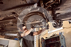 Repair man fixing car in repair station under lifted car during repair in garage