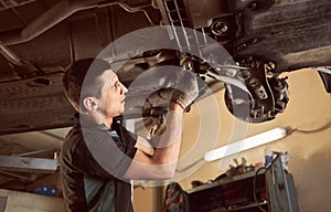 Repair man fixing car in repair station under lifted car during repair in garage