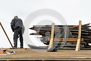 Repair of an old wooden roof. Carpenter with tools on the roof against the sky. A professional worker in a protective uniform