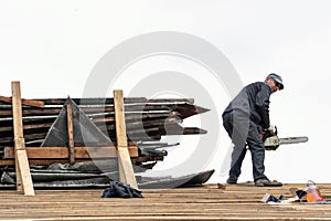 Repair of an old wooden roof. Carpenter with tools on the roof against the sky. A professional worker in a protective uniform