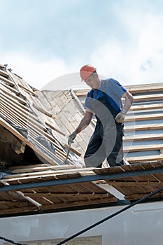 Repair of an old wooden roof. Replacement of tiles and wooden beams in an old house. A carpenter with tools in his hands is on the