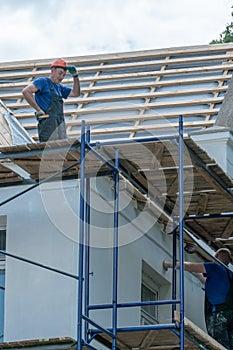 Repair of an old wooden roof. Replacement of tiles and wooden beams in an old house. A carpenter with tools in his hands is on the