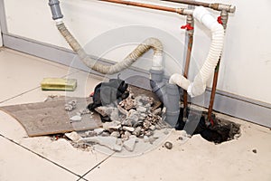 Repair plastic polypropylene gray sewer pipes in the hole in brick floor with broken tiles. Concept of pipe replacement, water