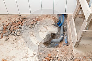 Repair plastic polypropylene gray sewer pipes in the hole in brick floor with broken tiles. Concept of pipe replacement, water