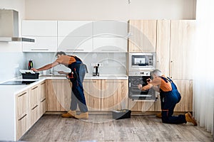 Repair. Two handymen, workers in uniform fixing, installing furniture and equipment in the kitchen, using screwdriver