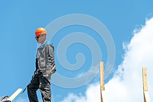 Repair of a wooden roof outdoors on a summer day against the background of blue sky and clouds. A carpenter in special clothes and