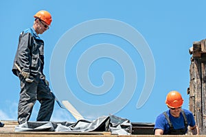 Repair of a wooden roof outdoors on a summer day against the background of blue sky and clouds. A carpenter in special clothes and