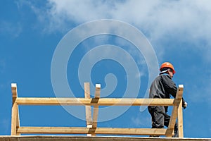 Repair of a wooden roof outdoors on a summer day against the background of blue sky and clouds. A carpenter in special clothes and