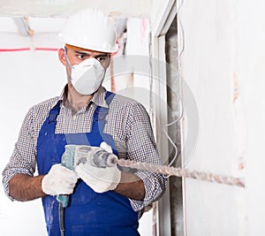 Repairer in helmet is perforating wall with drill