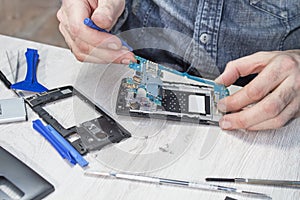 Repairing the mobile phone. The man`s hands take out the circuit board from the cell phone casing.