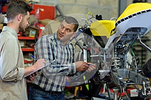 repairing motorcycle in workshop with coleague photo