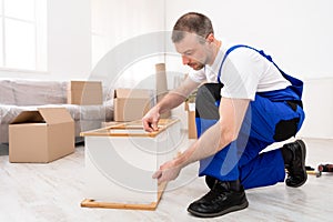 Repairman Assembling Furniture In Flat After Relocation, Wearing Blue Coverall