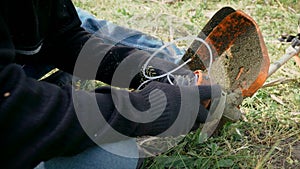 Repairman in black gloves and blue jeans fixing electric mower for cutting grass in garden