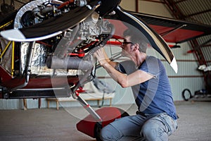 Repairman cheking engine in small aircraft from below.