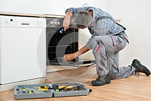 Repairman Examining Oven With Flashlight photo