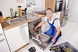 Repairman Fixing Dishwasher In Kitchen