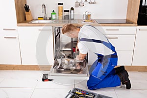 Repairman Fixing Dishwasher In Kitchen