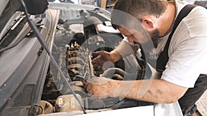 Repairman fixing engine of car and talking by phone at auto service. Mechanic works under hood of vehicle and consults