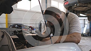 Repairman fixing engine of car and talking by phone at auto service. Mechanic works under hood of vehicle and consults