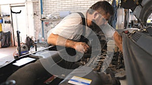 Repairman fixing engine of a car at workshop or service. Professional auto mechanic works under hood of vehicle. Bearded