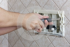 Repairman hands unscrewing a screw flush toilet box to fix bathroom closeup