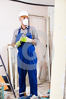 Repairman in helmet is perforating wall with drill