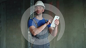 The repairman holds a tablet in his hands. A man in an unfinished building. An employee of a construction company in a