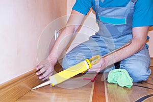 Repairman Installing Skirting Board Oak Wooden Floor with Caulking Gun Silicone