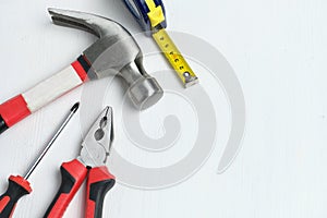 Repairman intruments hammer, screwdriver, measuring tape on white wooden background with copy space and top view