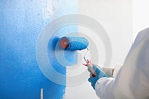 Repairman painting white wall in apartment blue using roller closeup