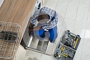 Repairman Repairing Dishwasher In Kitchen