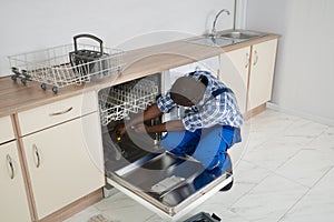 Repairman Repairing Dishwasher In Kitchen