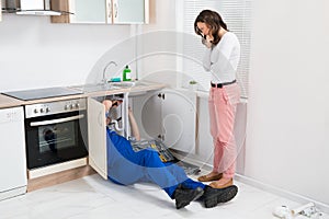 Repairman Repairing Pipe While Woman In The Kitchen