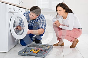 Repairman Repairing Washer In Front Of Woman