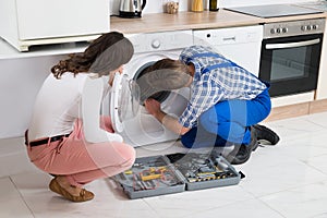 Repairman Repairing Washer In Front Of Woman