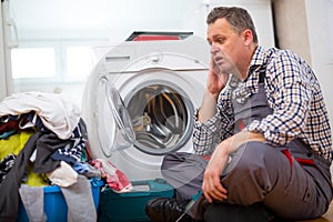 Repairman Repairing Washer In Kitchen, Sitting Next To Dirty Laundry